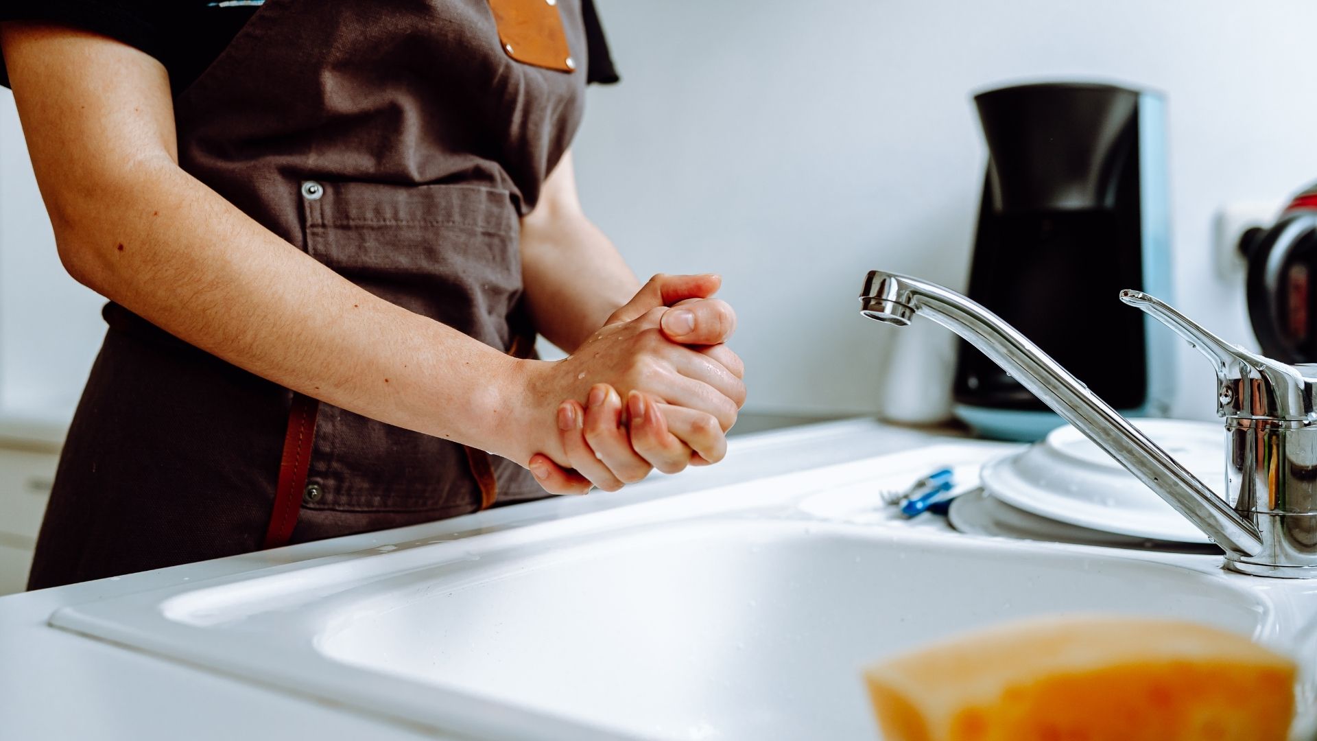 A person washing dishes with running water